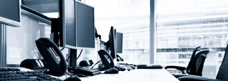 Schreibtisch mit mehreren Computermonitoren und einer Tastatur.