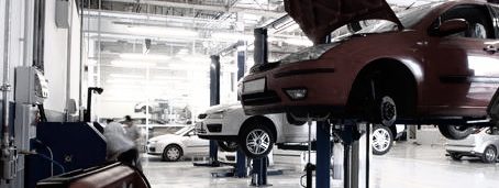 Werkstatt mit mehreren Fahrzeugen, einige auf Hebebühnen, andere in Reparatur.