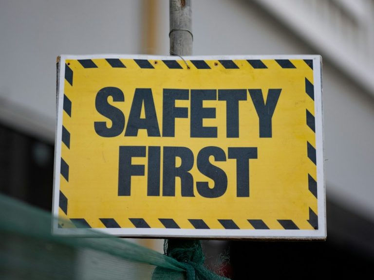 Gelbes Schild mit schwarzer Aufschrift "SAFETY FIRST", umrandet von schwarzen und gelben Streifen.